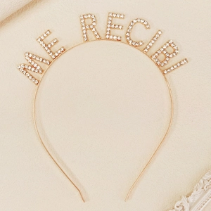 Detailed close-up of ME RECIBI rhinestone lettering on a golden graduation headband