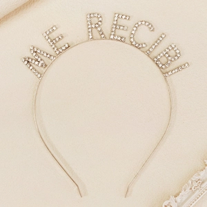 Detailed view of silver hairband with ME RECIBI! rhinestone lettering on leather background
