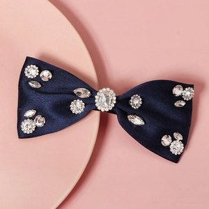 Detailed close-up of navy blue satin bow hair clip with sparkling rhinestones on pink background