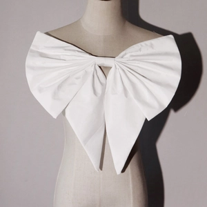 Detail view of large white handmade bow accessory with long trailing ribbon on dress form