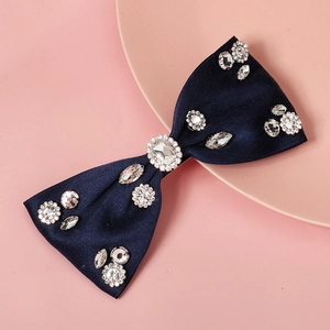 Navy blue satin bow hair clip with sparkling rhinestones on a soft pink background