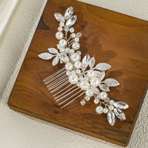 Close-up of bridal hair comb with white pearls, crystals and silver metal leaves on wood