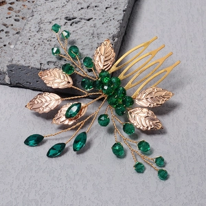 Handmade gold leaf hair comb featuring deep green crystal beads on a grey stone surface