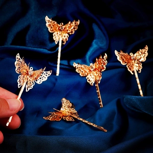 Set of five gold hollow butterfly hair clips with crystals on a deep blue satin background