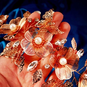 Macro detail of gold petal hairpiece with pearls and crystals on blue fabric