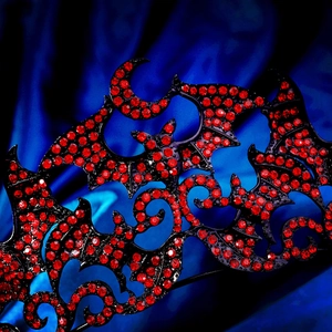 Close-up of gothic crown with black bats and red rhinestones on blue silk fabric