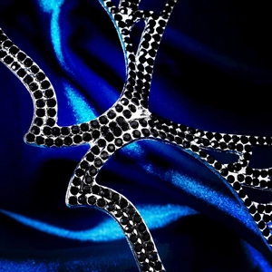 Detailed close-up of premium silver metal mask with black rhinestones on blue silk
