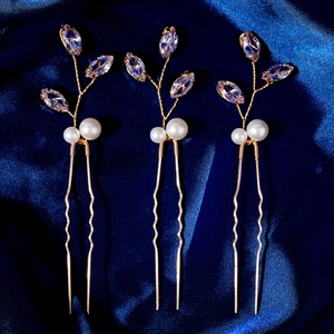 Détail de trois épingles à cheveux dorées avec zircons et perles sur de la soie bleue