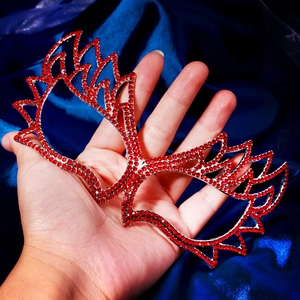 Detailed view of red rhinestone masquerade mask with wing design held by hand