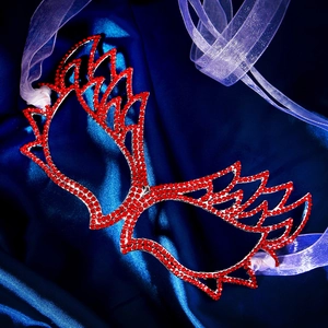 Close-up of red rhinestone masquerade mask with wing design on blue satin fabric