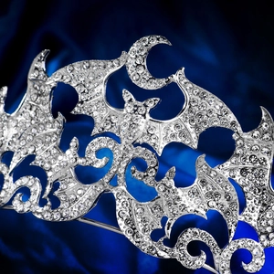 Detail of silver bat and crescent moon crown with rhinestones on blue silk background