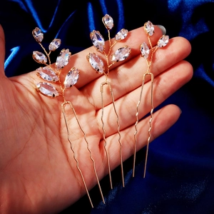 Detail of three gold leaf hair pins with clear marquise stones on blue silk fabric