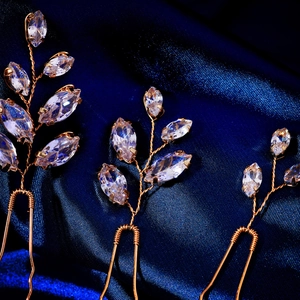 Macro detail of three gold leaf hair pins with marquise cut zircon on blue silk