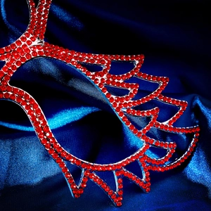 Macro detail of red rhinestone masquerade mask on blue satin fabric background