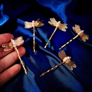 Detailansicht goldener Libellen-Haarspangen mit Perlen auf dunkelblauem Seidenstoff
