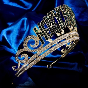 Gros plan d'une couronne dorée avec lettres SASHAY en strass vert sur satin bleu