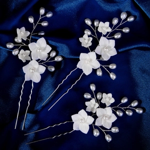 Detail of white resin flower hair pins with pearls on blue satin for bridal styling