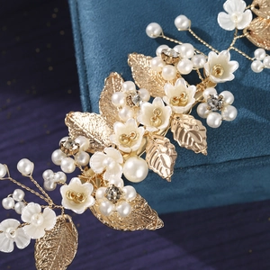 Macro detail of bridal hair clip with gold leaves, white resin flowers and pearls