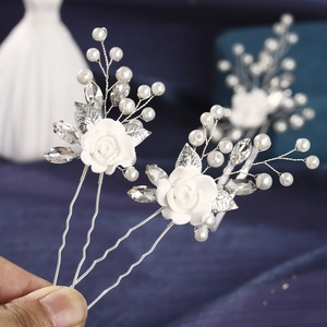 Detailed close-up of white ceramic rose hairpins with pearls and silver leaves