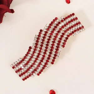 Macro detail of wave-shaped hair clip with red and white rhinestones on textured surface