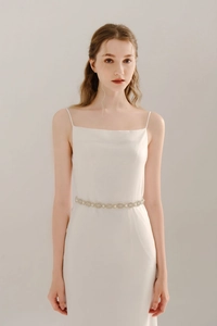 Close-up of elegant bridal belt with rhinestones and pearls on a white satin dress