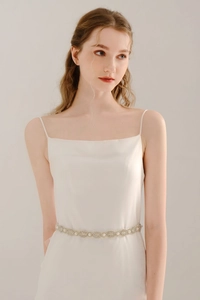 Detailed view of elegant bridal sash with pearls and rhinestones on a white satin dress