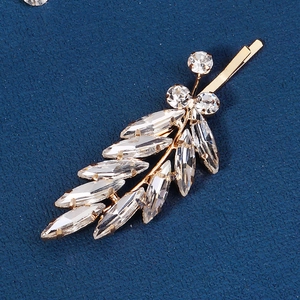 Macro shot of gold leaf-shaped hair clip featuring marquise rhinestones on blue fabric