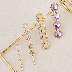 Detail of four gold hair clips with purple crystals and rhinestones on a display stand