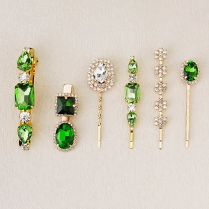 Detailed view of six gold-plated hair clips with emerald green crystals and rhinestones