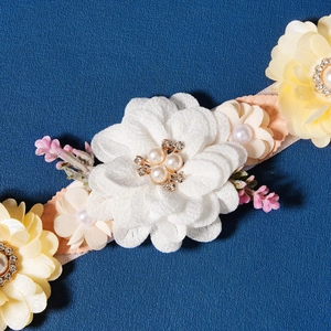 Detail of bridal floral belt featuring white fabric flowers, pearls, and rhinestones