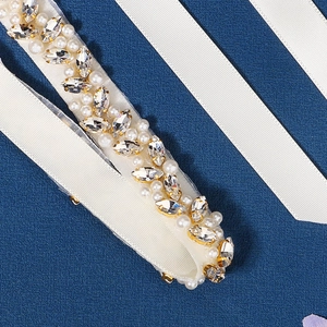 Detailed macro view of white pearls and golden marquise rhinestones on a bridal sash