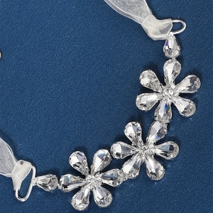Detail van bruidshoofdband met kristallen bloemen en witte organza linten