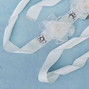 Detail of white satin bridal belt featuring delicate mesh flowers and sparkling crystals