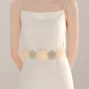 Détail de la ceinture à fleurs en strass sur une robe de maternité blanche pour photos
