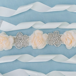 Détail d'une ceinture de maternité avec fleurs en strass et roses en tissu sur ruban blanc