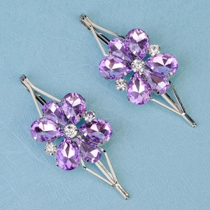 Close-up of two purple crystal flower hair clips with silver metal bases on blue background