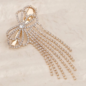 Detailed close-up of golden bow hair clip with sparkling rhinestones and elegant long tassels