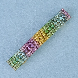 Macro detail of rainbow gradient crystal rhinestones on a rectangle gold hair clip