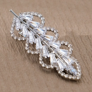 Close-up of a silver leaf-shaped hair clip with sparkling baguette and round zircon stones