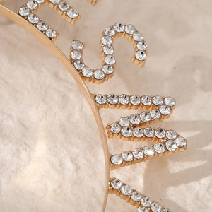 Macro view of gold-tone metal headband featuring pave-set rhinestones and letter shapes