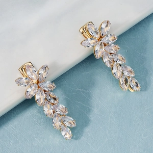Détail de boucles d'oreilles pendantes dorées avec zircons marquise sur fond de marbre