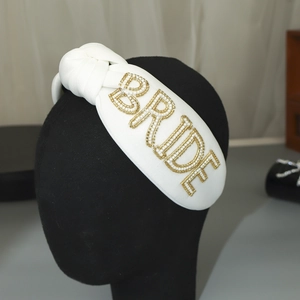 Close-up of a white padded bridal headband with beaded BRIDE lettering and a top knot