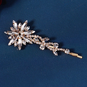Close-up of golden rhinestone flower hair clip with marquise-cut crystals on blue background