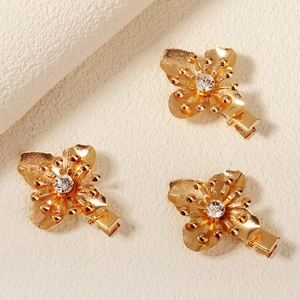 Detaillierte Ansicht von drei goldenen Blumen-Haarspangen mit gebürsteter Textur und Strass
