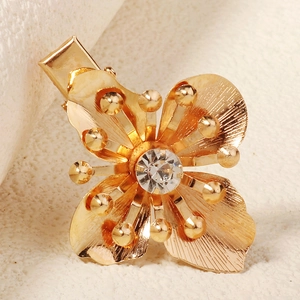 Makro-Detail einer goldenen Blumen-Haarklammer mit glitzerndem Strass und Struktur-Blüten