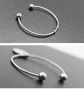 Detalle de brazalete abierto de acero inoxidable plateado con puntas de bola y perlas