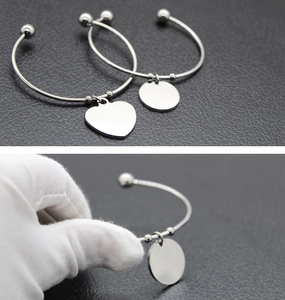 Primer plano de pulsera rígida de acero pulido con colgante de corazón y redondo