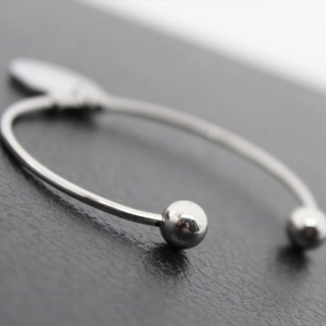 Brazalete de herradura de acero pulido con puntas esféricas y un colgante de corazón