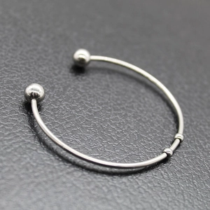 Anillo abierto de acero inoxidable plateado con cuentas decorativas sobre fondo texturizado