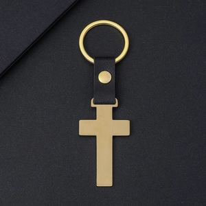 Porte-clés croix en métal doré avec lanière en cuir noir sur fond texturé élégant